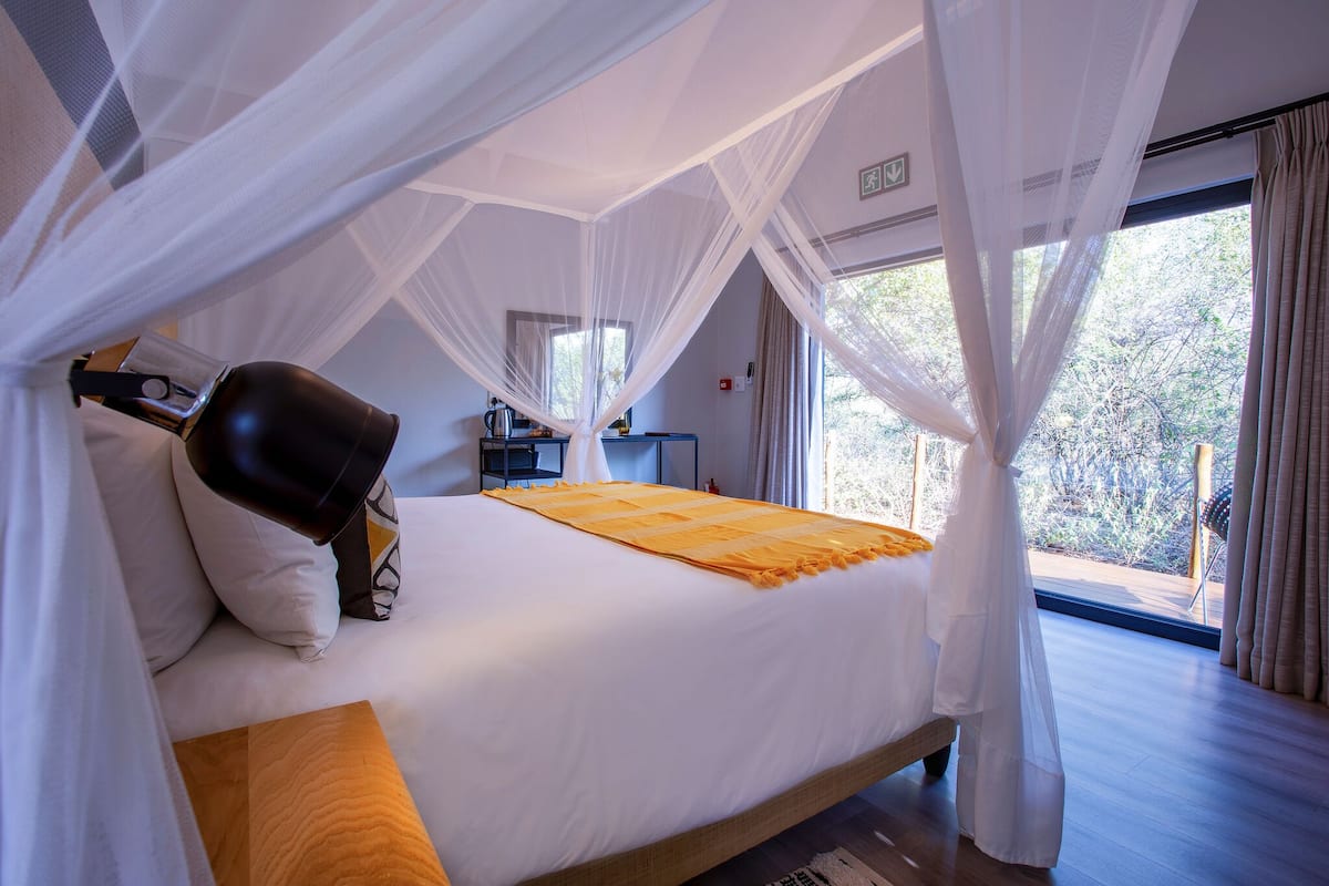 A room with a bed, white curtains, and a view of trees.
