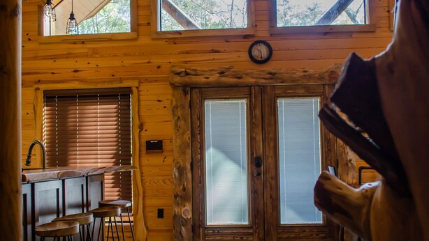 A wooden cabin interior with a kitchen area, bar stools, and large windows. - Family friendly cabin with an exclusive view of a waterfall on the Okatoma River (Seminary)