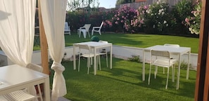 A patio with white tables and chairs, surrounded by a well-maintained lawn and flowering plants. - La Smeralda - Boutique Rooms and Breakfast (Golfo Aranci)
