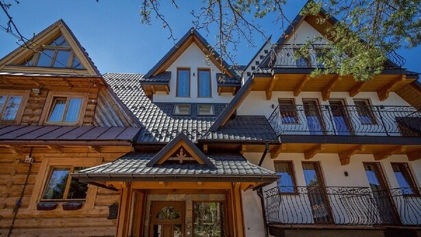 A multi-story log cabin with a steeply pitched roof, wooden exterior, and a balcony with wrought iron railings.