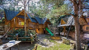 A wooden cabin with a green slide, surrounded by trees and a picnic table.