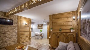 A cozy room with wooden walls, a stone accent wall, a dining area with a table and chairs, and a sofa with a throw pillow.