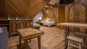 A cozy attic bedroom with wooden beams, a bed, a small table, and a TV mounted on the wall.