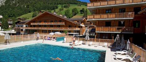 Un bâtiment en bois avec une piscine et des chaises longues.