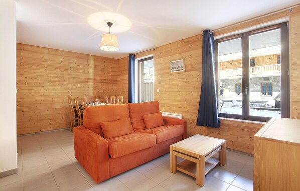 Une pièce avec un plancher en bois, un canapé en bois, une petite table en bois et une grande fenêtre avec des rideaux.