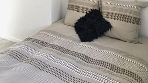 Une chambre à coucher avec un lit, deux oreillers, un plaid noir et un miroir hexagonal fixé au mur.
