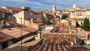 Vue d’une ville historique, avec ses toits couverts de tuiles en terre cuite, un imposant beffroi et un mélange de bâtiments résidentiels et commerciaux.