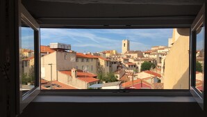 Une fenêtre donnant sur un paysage urbain, avec des bâtiments aux toits recouverts de tuiles rouges et une tour imposante.