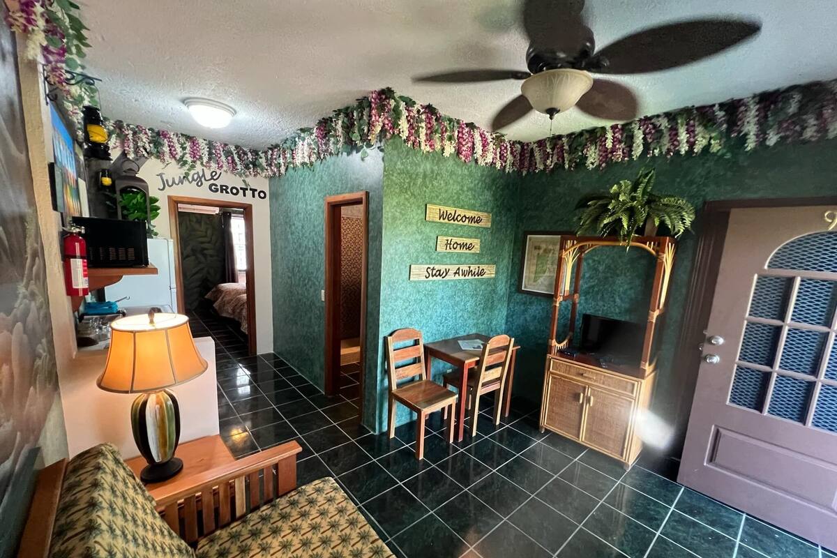 A room with a sofa, a dining table with chairs, a ceiling fan, and a TV on a wooden cabinet.