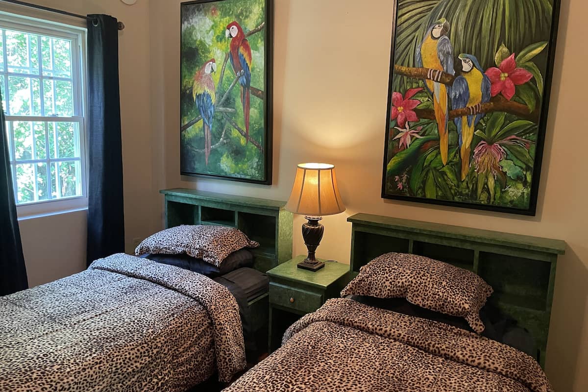 A room with two beds, each with leopard print bedding, a nightstand with a lamp, and two paintings of parrots on the wall.