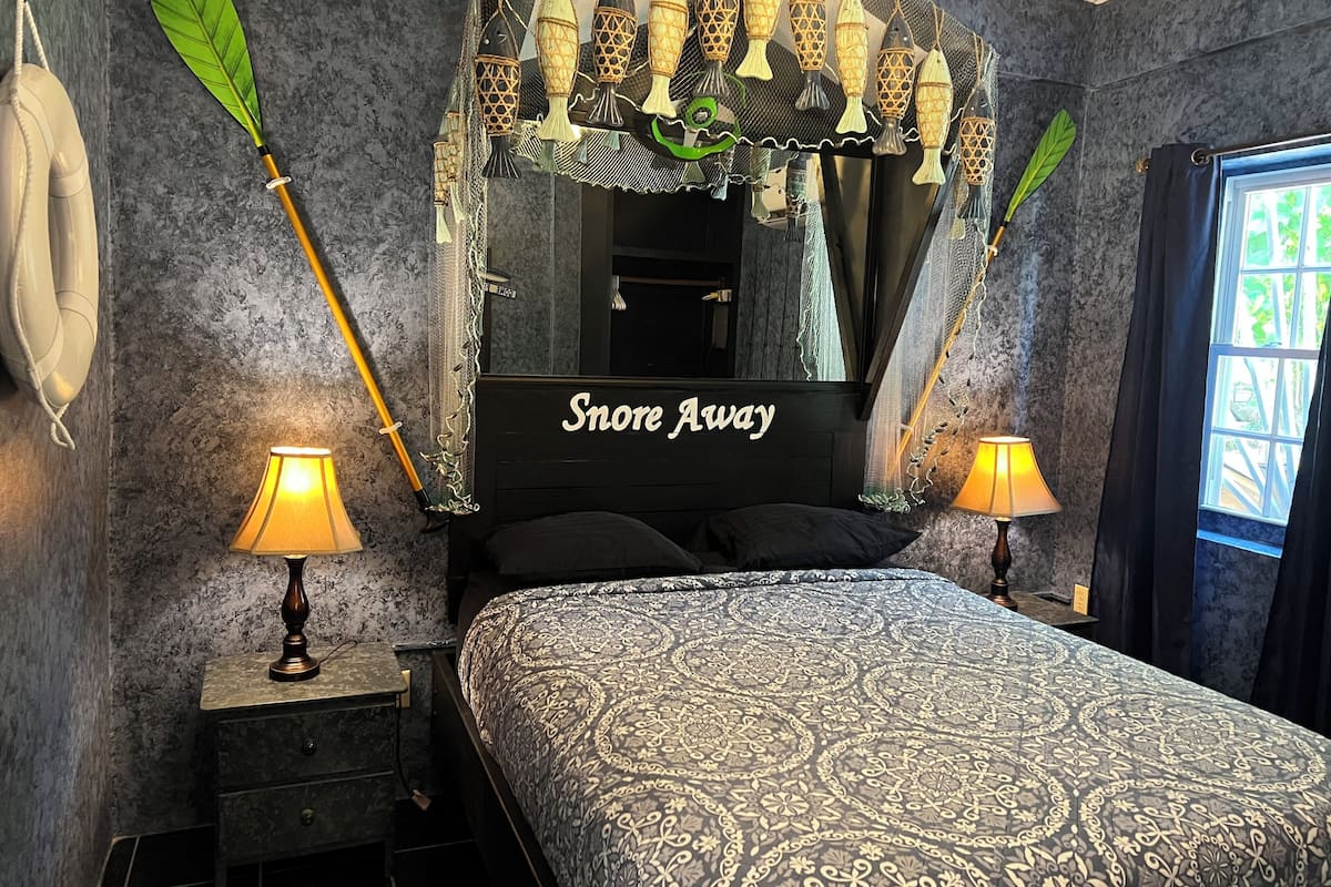 A bedroom with a bed, two bedside lamps, a mirror, and a decorative fish wall hanging.