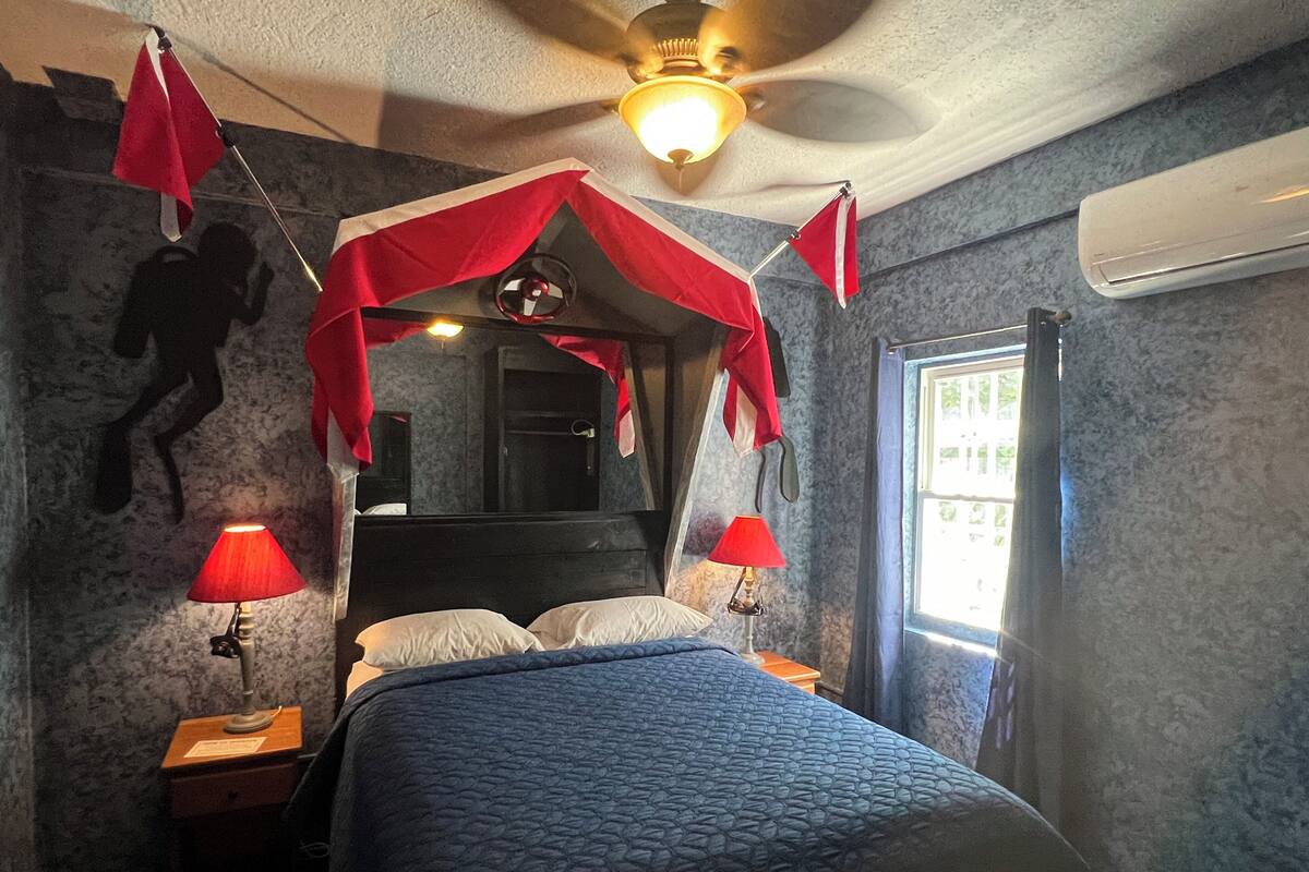 A bedroom with a four-poster bed, two bedside lamps, a ceiling fan, and a window with curtains.
