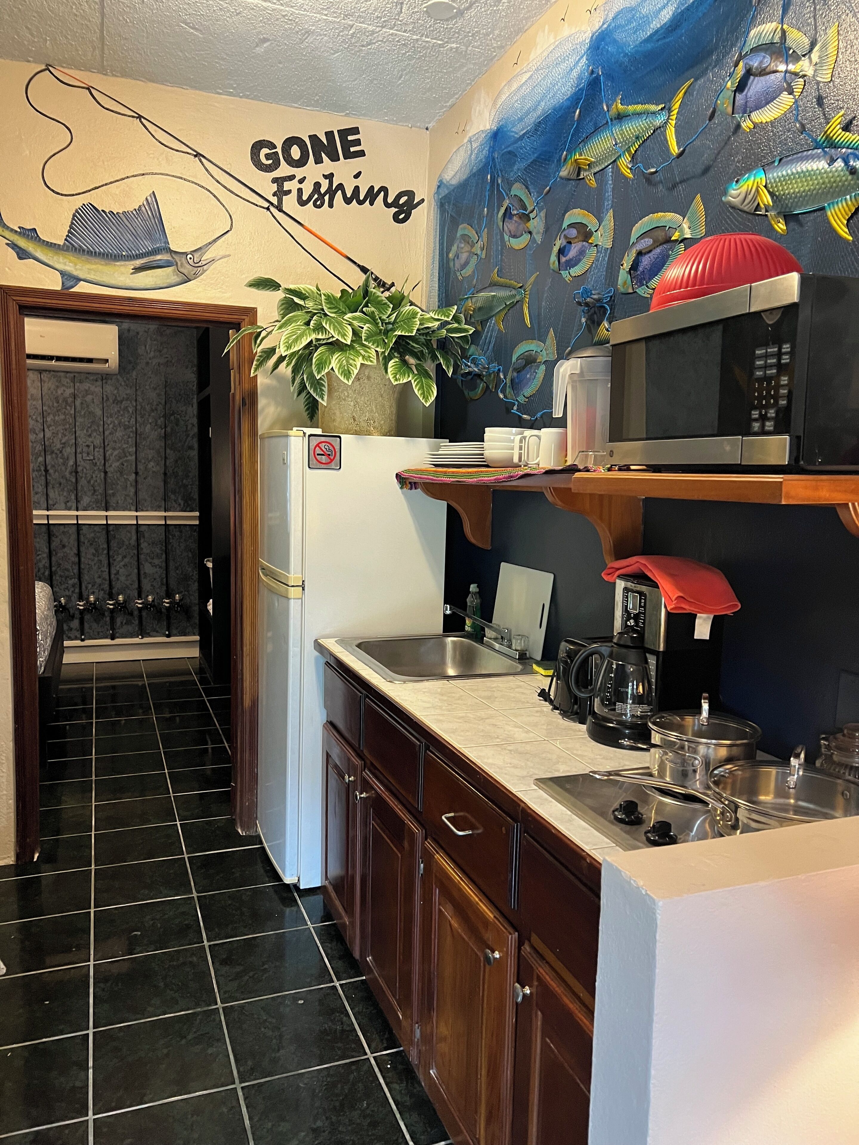 A kitchen with a sink, stove, and microwave. There is a sign on the wall that says "Gone Fishing."