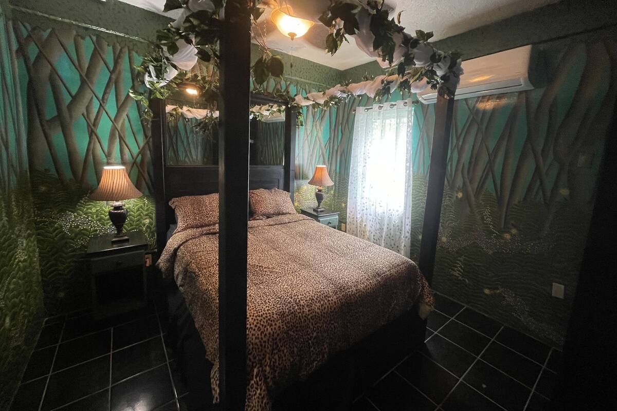 A bedroom with a canopy bed, green walls, and a patterned bedspread.