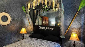 A bedroom with a bed, two bedside lamps, a mirror, and decorative fish hanging above the bed. - Belize Budget Suites (San Pedro)