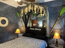 Een slaapkamer met een bed, twee bedlampen, een spiegel en decoratieve vissen die boven het bed hangen.