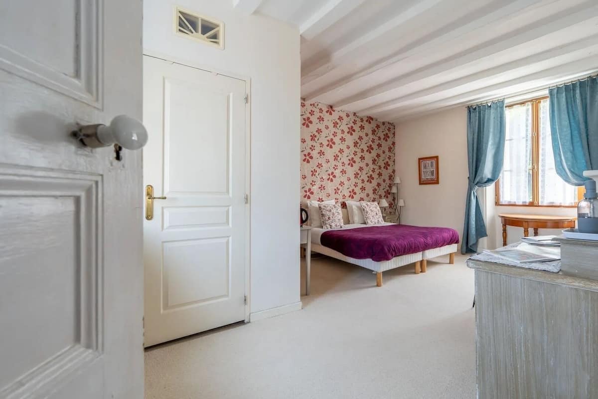 A bedroom with a bed, a desk, and a window with curtains.