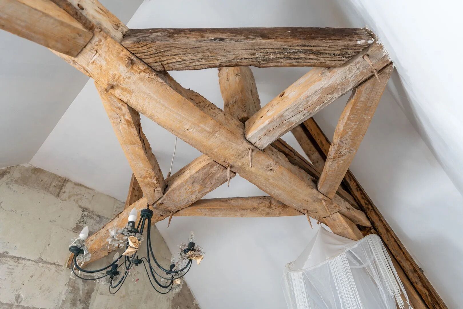 Een plafond met zichtbare houten balken en een kroonluchter.