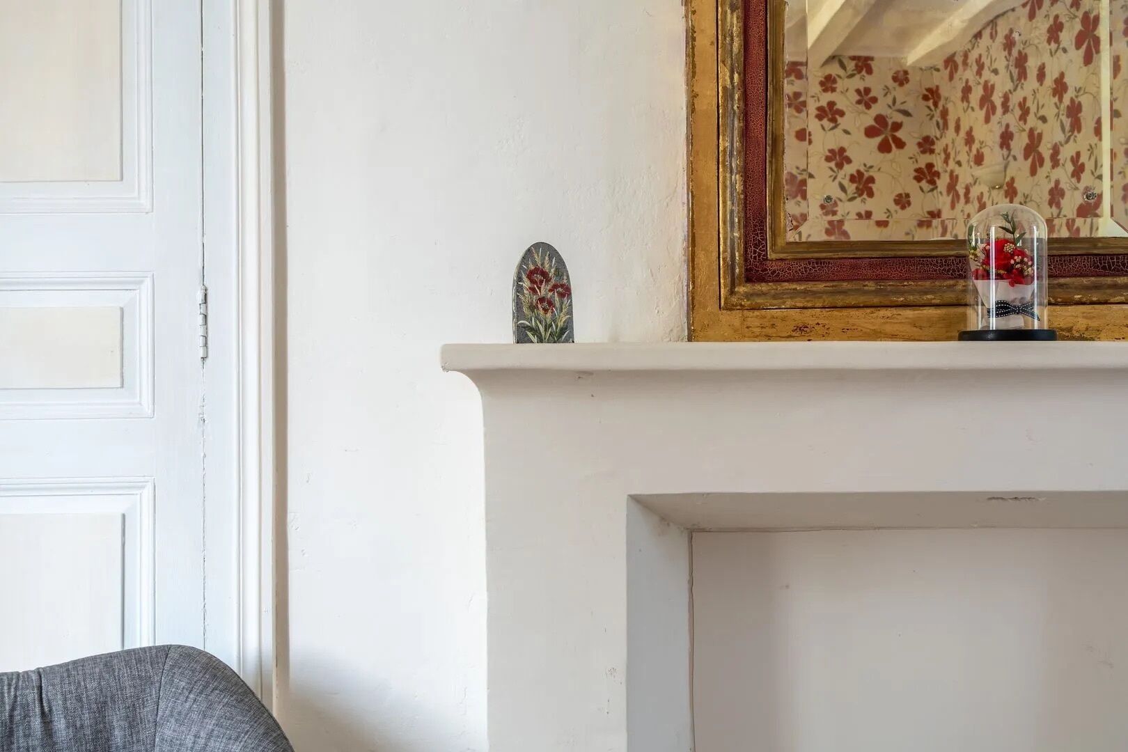 Une cheminée blanche surmontée d’un miroir orné de motifs floraux.