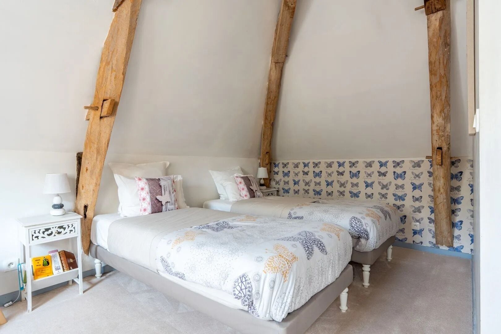 A bedroom with two beds, wooden beams, a white nightstand, and a patterned wall.