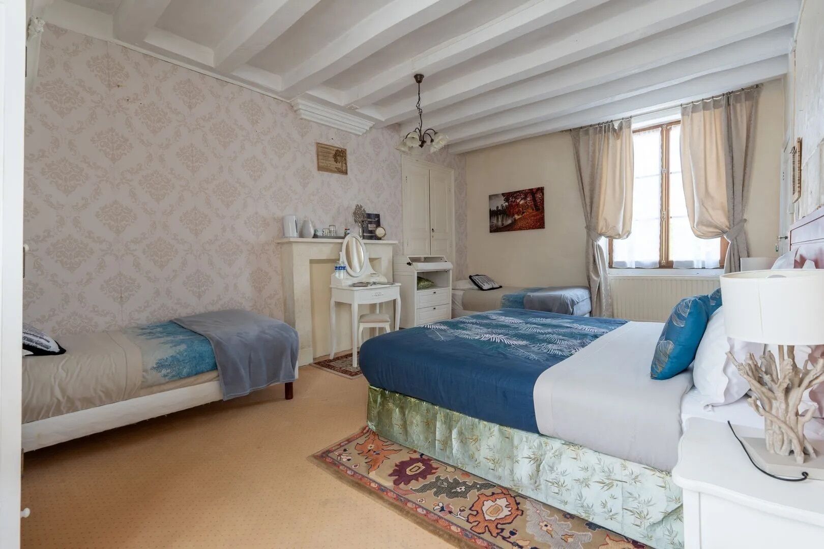 Een slaapkamer met twee eenpersoonsbedden, een bureau, een stoel, een spiegel, een raam met gordijnen en een decoratieve lamp.