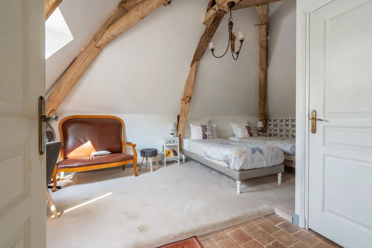 A cozy attic bedroom with a sloped ceiling, a wooden chair, a bed with patterned bedding, and a small side table.
