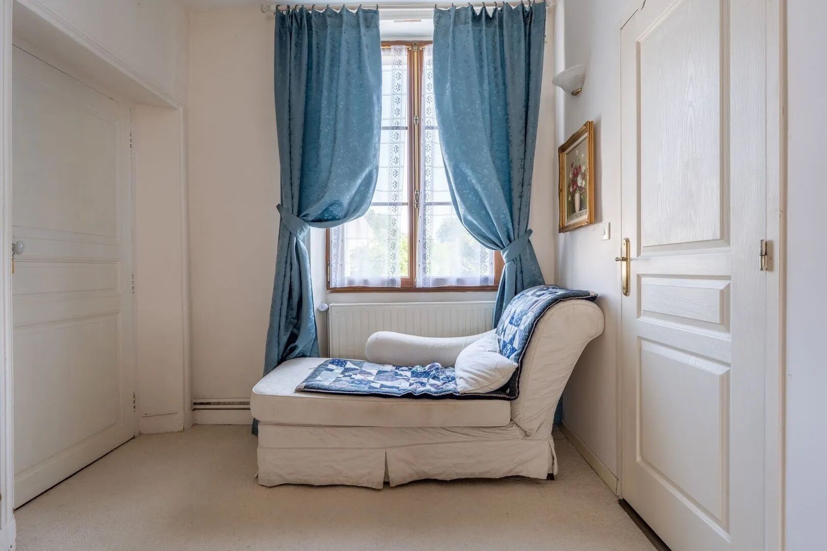 A small, cozy room with a single bed, a radiator, and a window with blue curtains.