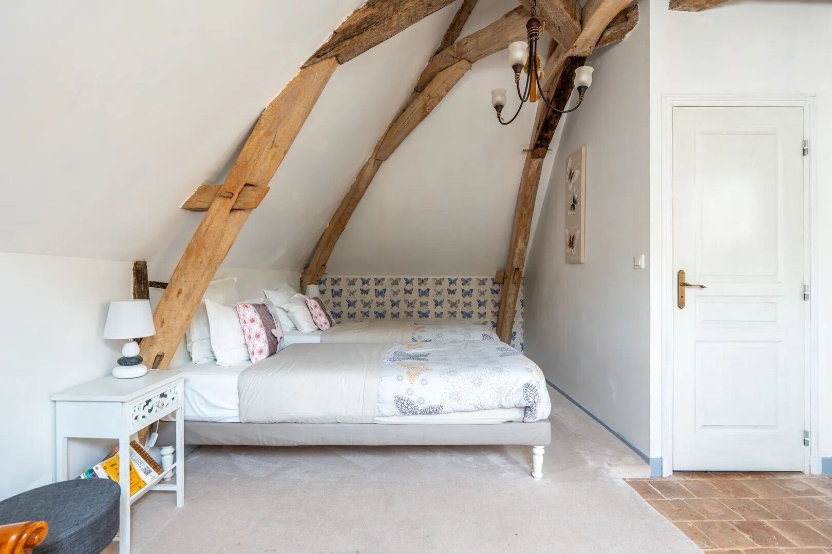 A bedroom with a sloped ceiling, a bed with patterned bedding, a bedside table with a lamp, and a door with a brass handle.