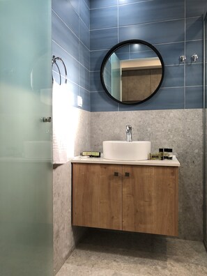 Un baño con un lavabo blanco, tocador de madera y un espejo redondo.