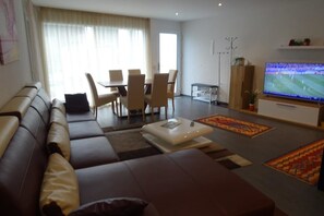 A modern living room with a sofa, dining table, chairs, a TV, and a coffee table.