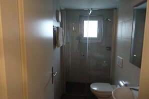 A small, compact bathroom with a toilet, sink, and glass shower enclosure.