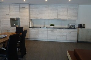 A modern kitchen with light wood cabinets, a built-in oven, and a dining area with a wooden table and chairs. - Bahnhofplatz Apartment (Interlaken)