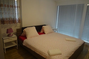 A bedroom with a bed, a nightstand, a lamp, and a window with blinds.