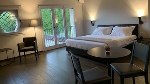 A bedroom with a large bed, a desk, a chair, a table, and a window with a view of trees. - Palazzo Dè Rossi Hotel (Sasso Marconi)