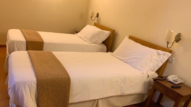 A hotel room with two beds, each with white linens and a brown throw blanket. There is a wooden nightstand with a telephone and a remote control. - Palazzo Dè Rossi Hotel (Sasso Marconi)