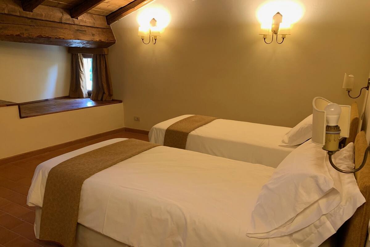 A hotel room with two beds, wooden beams on the ceiling, and wall-mounted lights.