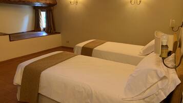 Une chambre d’hôtel avec deux lits, des poutres en bois au plafond et des lampes fixées au mur.