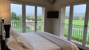 A bedroom with a large bed, a TV mounted on the wall, and a balcony with a view of the countryside. - Palazzo Dè Rossi Hotel (Sasso Marconi)