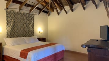 A bedroom with a wooden ceiling, a bed with white and red bedding, a nightstand, a wall-mounted lamp, and a television on a wooden stand.