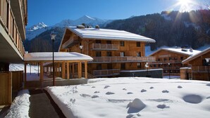 Eine Holzhütte mit Balkonen und verschneitem Gelände, vor einer Bergkulisse.