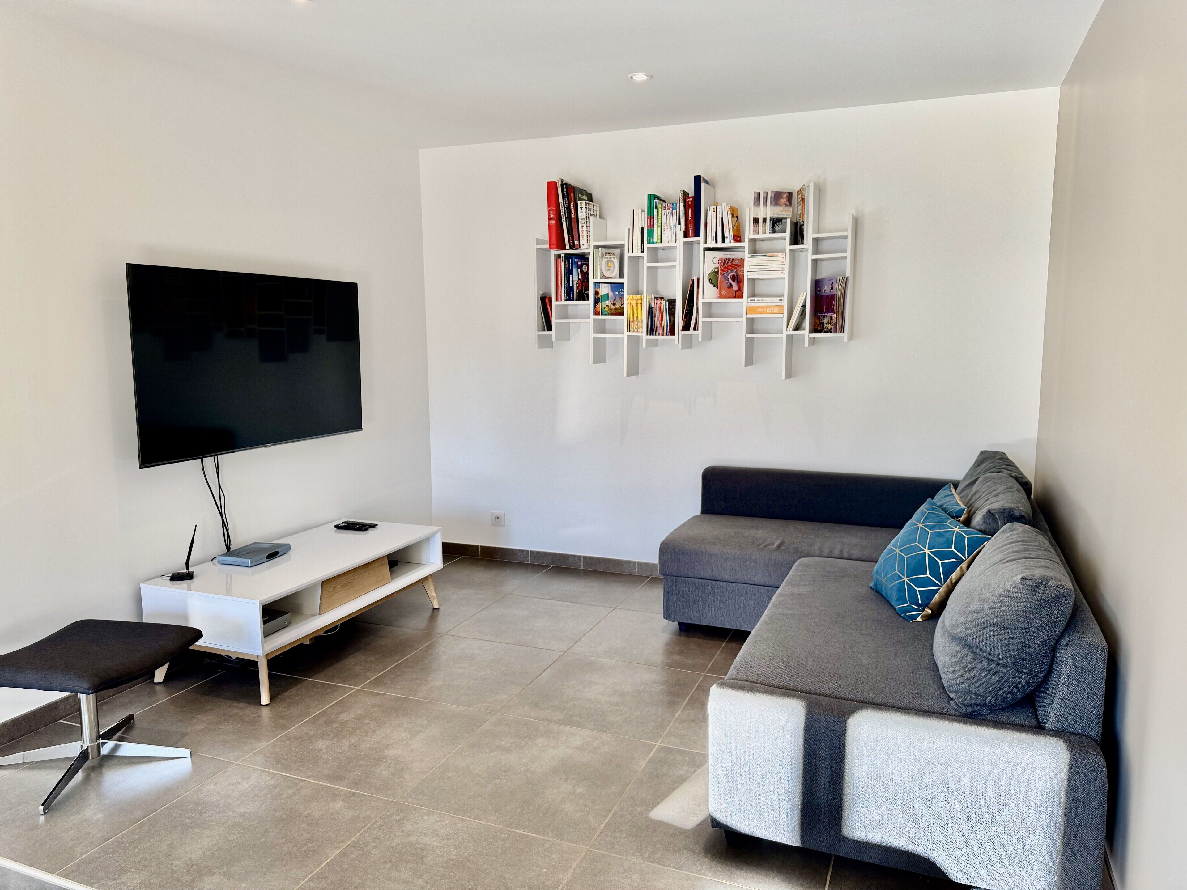 Un salon moderne avec un téléviseur à écran plat, un canapé gris, un meuble de rangement blanc et une bibliothèque.