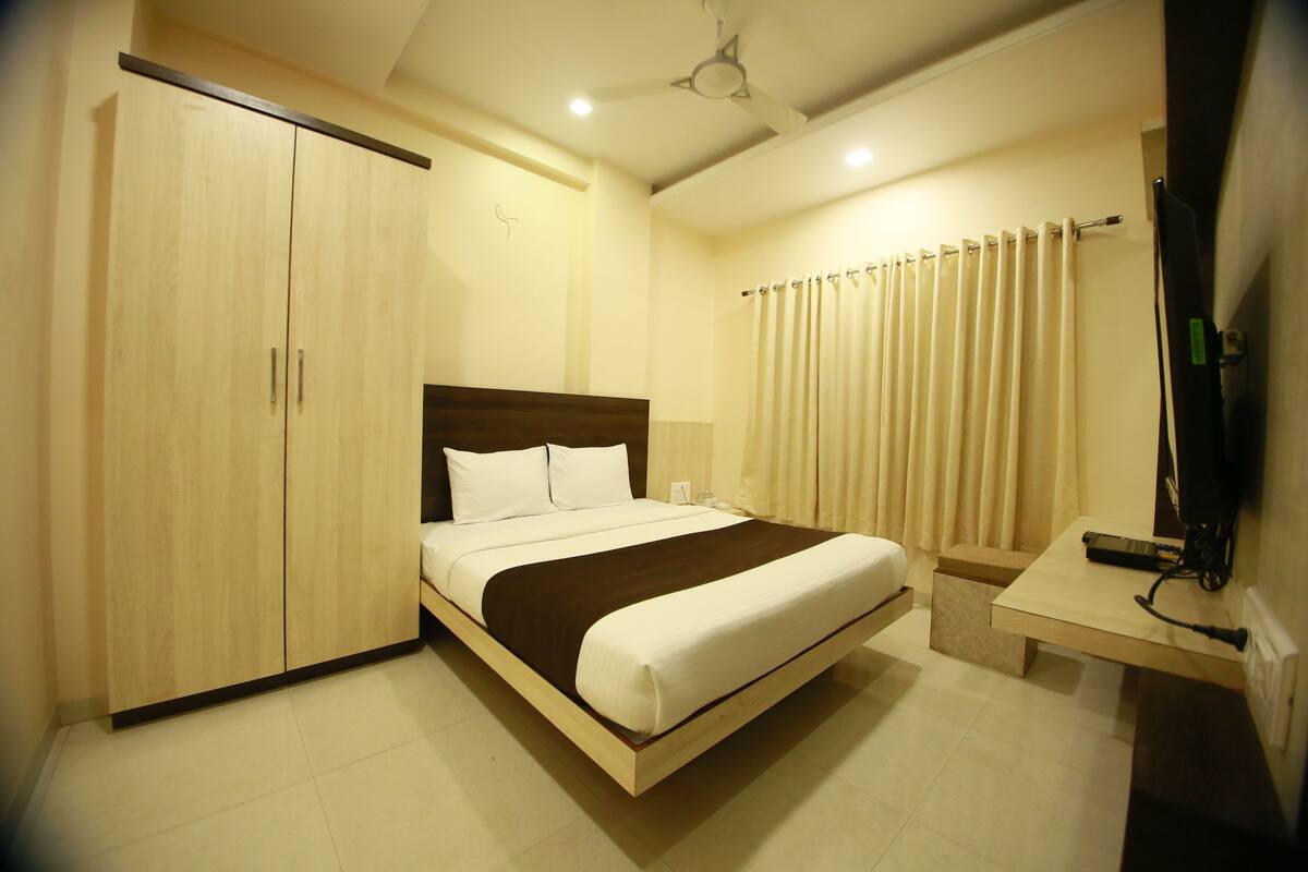 A hotel room with a bed, wardrobe, bedside table, and a television.