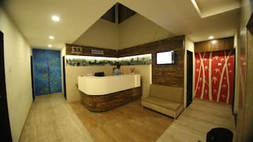 A reception area with a reception desk, a sofa, a wall with a tree mural, and a red wall with bamboo designs.