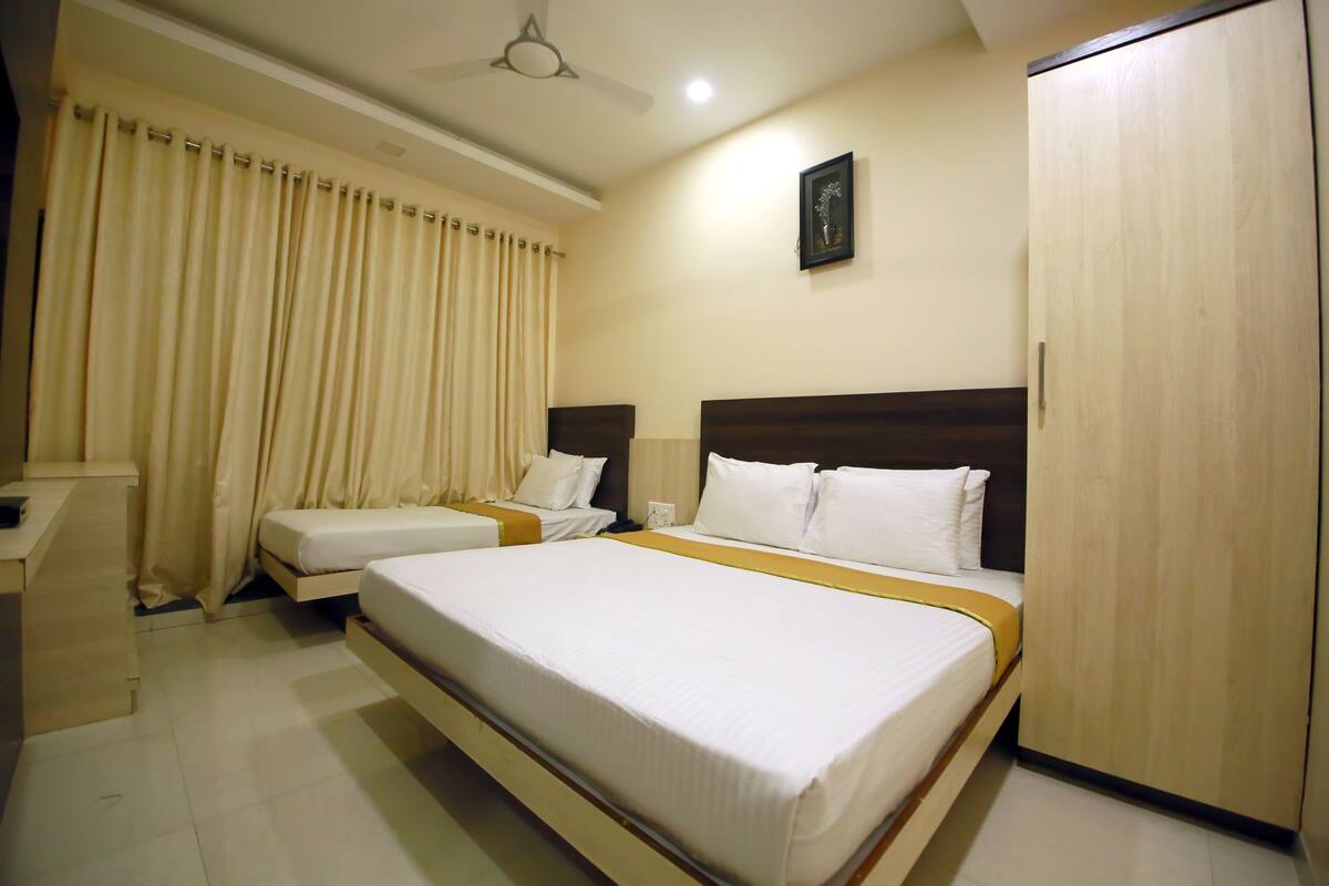 A hotel room with two single beds, a wardrobe, a desk, and a ceiling fan.