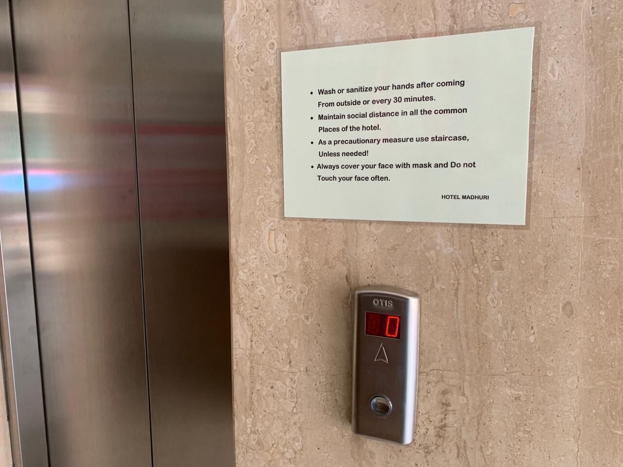 A wall-mounted sign with health and safety guidelines and a digital elevator control panel.