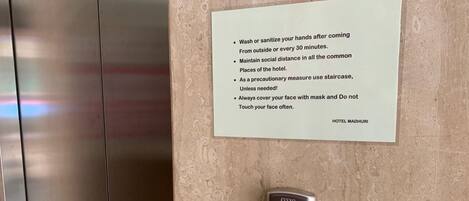 A wall-mounted sign with health and safety guidelines and a digital elevator control panel.