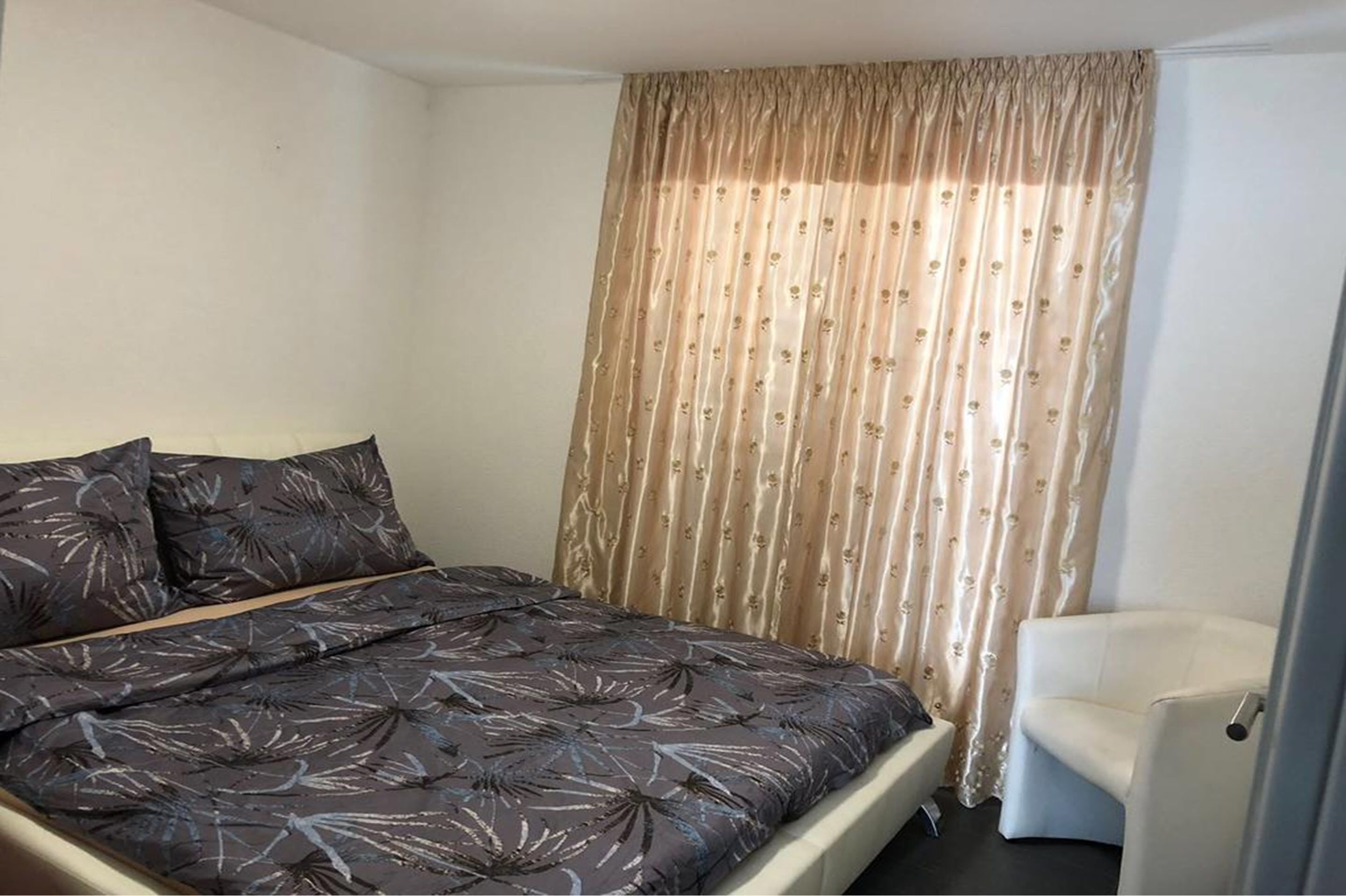 A bedroom with a bed, a chair, and a window with curtains.