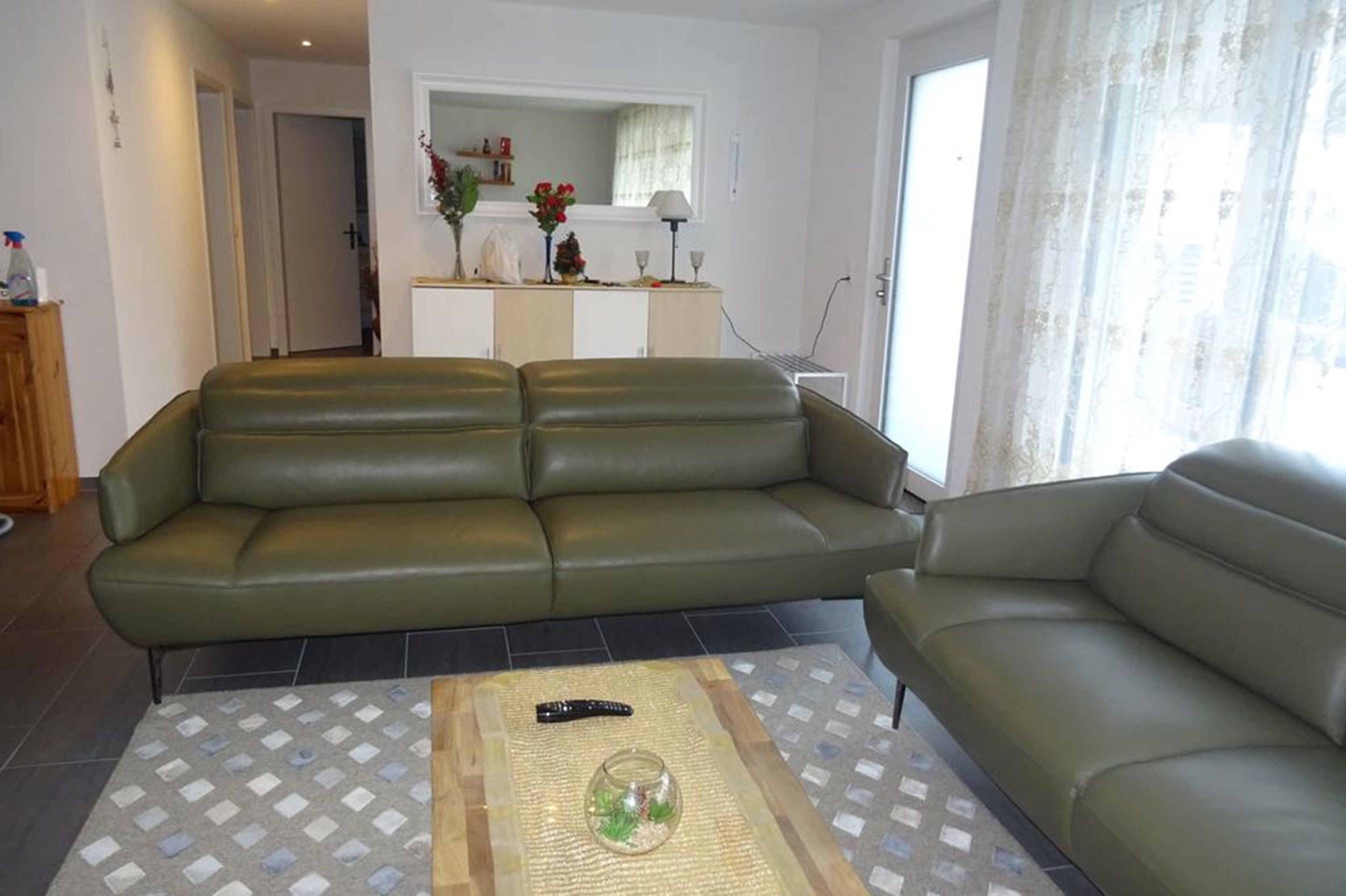 A living room with a green sofa, a small table with a glass container, and a white cabinet with decorative items.