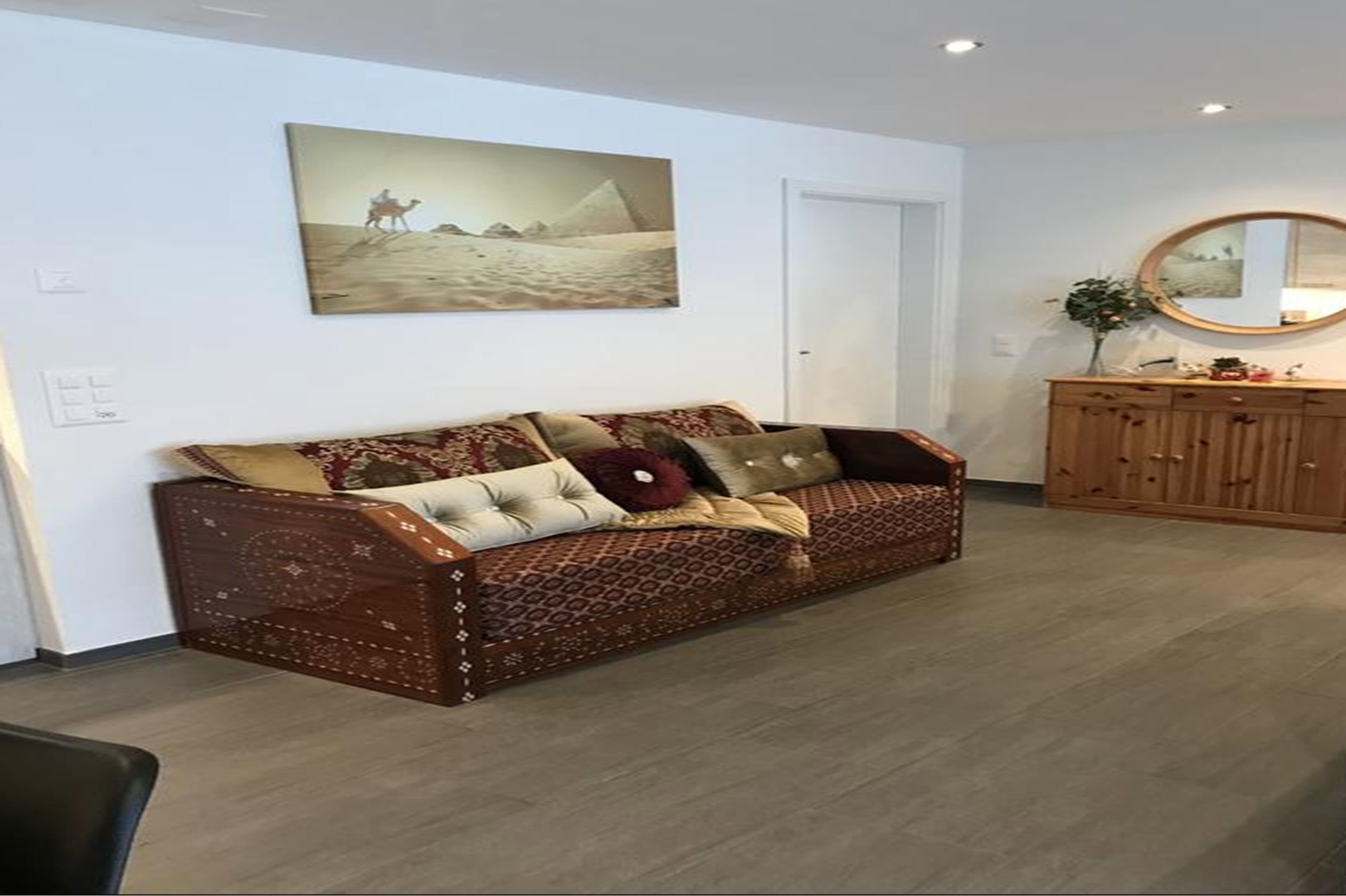 Una sala de estar con un sofá estampado, un cuadro en la pared y un aparador de madera.