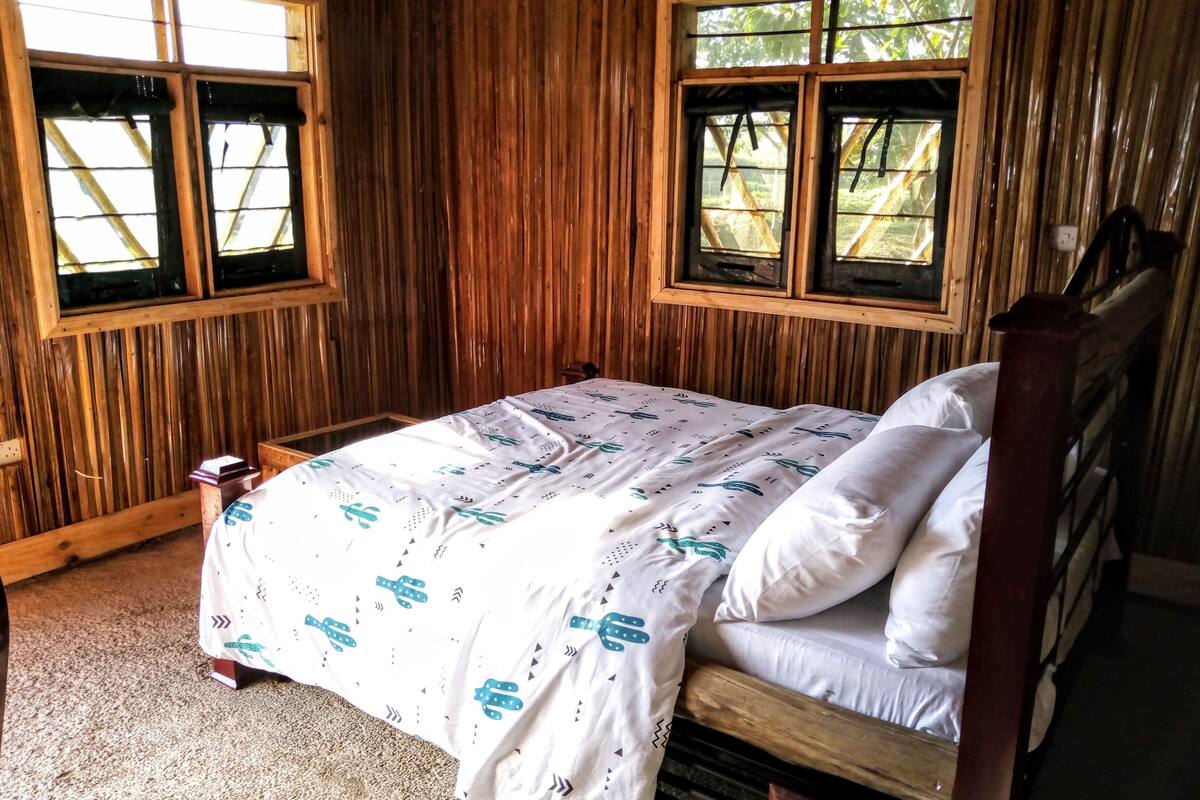 A wooden-paneled room with a bed, two windows, and a small table.